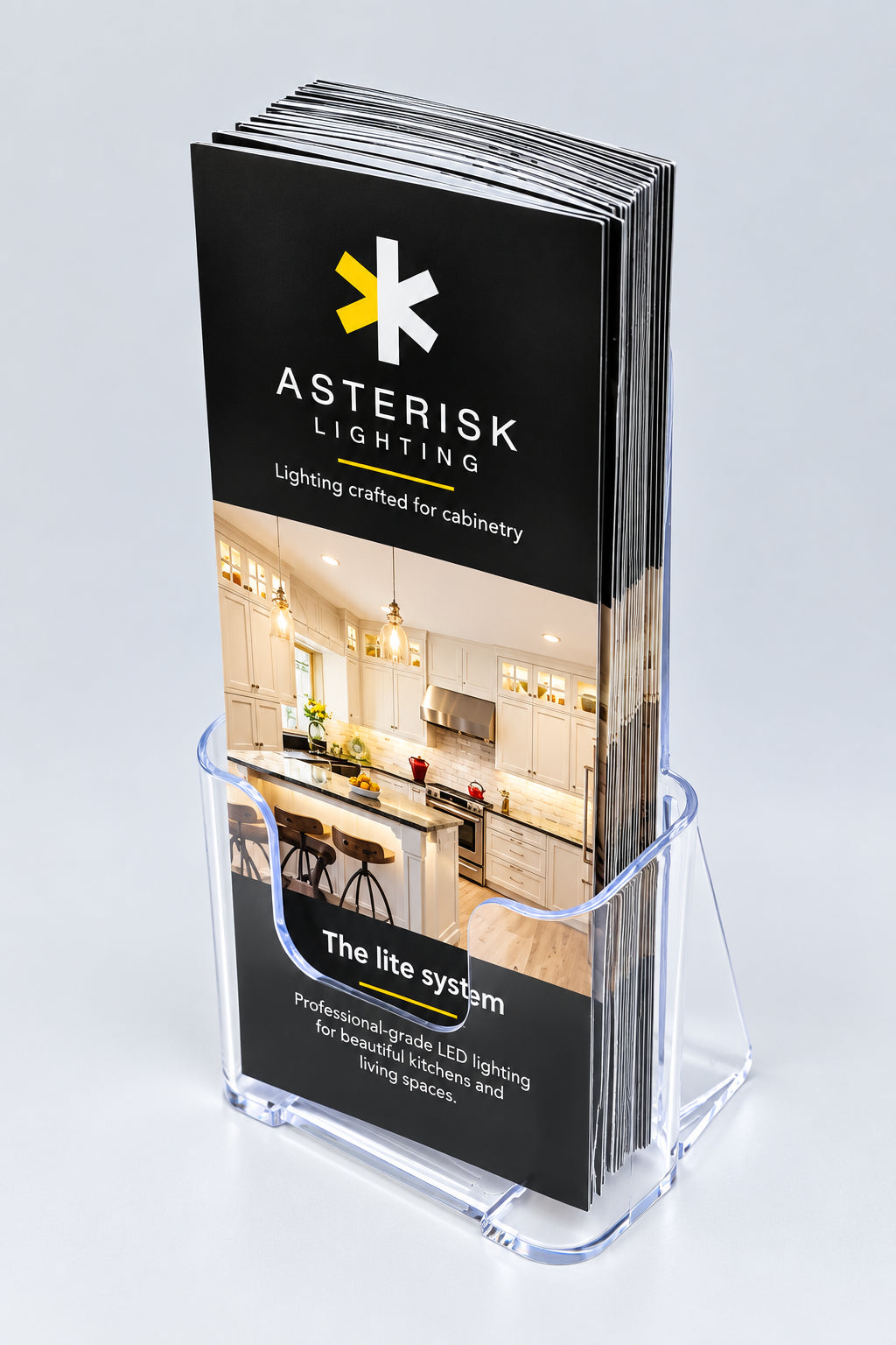A clear acrylic stand holding a stack of printed brochures for Asterisk Lighting, photographed on a clean light gray studio background.